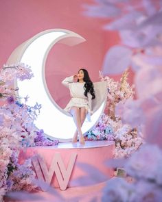 a woman sitting on top of a pink moon with flowers around her and the letter w