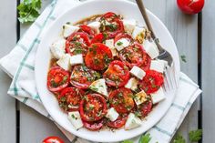 a white plate topped with sliced tomatoes and feta cheese on top of a wooden table