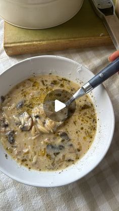 a person holding a spoon in a bowl of soup on a table next to a cutting board