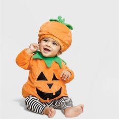 a baby in a pumpkin costume sitting on the floor