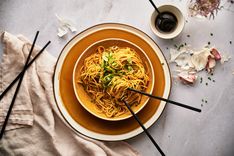 a bowl of noodles and chopsticks on a table next to an empty cup