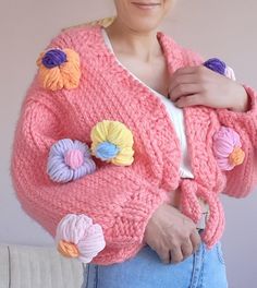 a woman wearing a pink cardigan with crocheted flowers on it