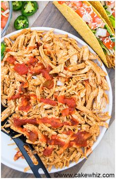 shredded chicken on a white plate with corn and salsa in the background, next to tortilla chips