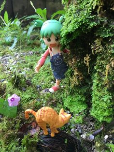 a doll is standing next to a cat figurine in the mossy ground