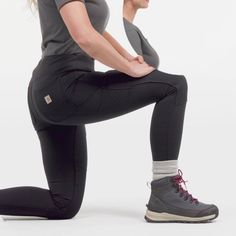 a woman squats on one leg while holding her hands behind her back and looking to the side