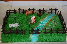 a birthday cake with horses on the grass and water in the middle, surrounded by wooden fence posts