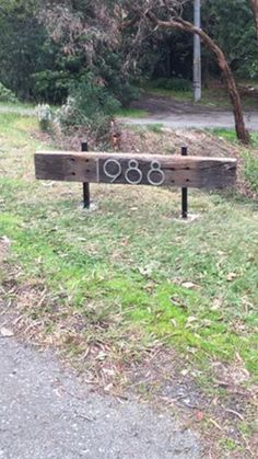 a wooden bench sitting on the side of a road near a park with trees and grass