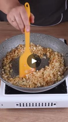 a person stirring food in a skillet on top of a stove with a yellow spatula