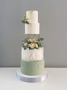 a three tiered white and green wedding cake with greenery on the top layer