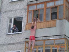 a man hanging off the side of a building with his arms in the air while another man looks out from an open window