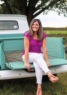 a woman sitting on the back of a pick up truck in front of a tree