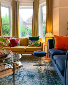 a living room filled with lots of furniture next to a window covered in yellow curtains