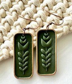 pair of earrings with green leaves on them sitting on top of a white cloth rug