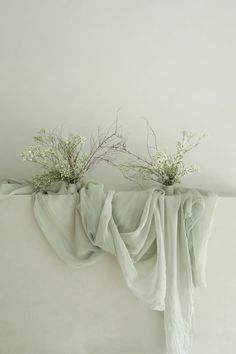 two vases with white flowers are sitting on a table cloth draped over the edge