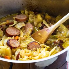 a pot full of cabbage and sausage with a wooden spoon in the bowl next to it