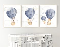 two paintings of hot air balloons in the sky above a crib with a baby's bed next to them