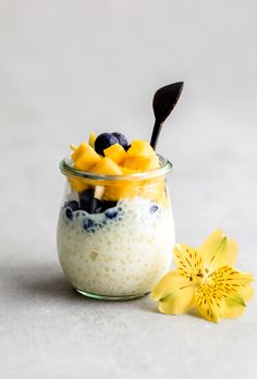 a glass jar filled with yogurt and blueberries next to a yellow flower