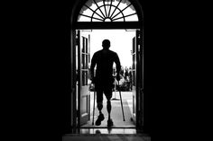 the silhouette of a man walking out of an open door with his cane in hand