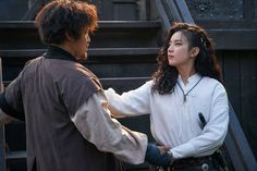 a man and woman standing next to each other in front of stairs with their hands together