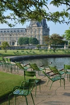 there are many green chairs in front of the water and a large building behind it