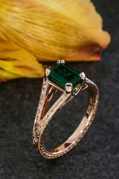 an emerald and diamond ring sitting on top of a table next to a yellow flower