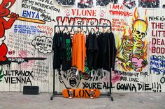 a skateboard sits in front of a wall with graffiti on it and clothes hanging up to dry