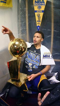 the basketball player is sitting in front of his trophy and pointing at it with one hand