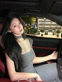 a woman sitting in the driver's seat of a car with her hand on the steering wheel