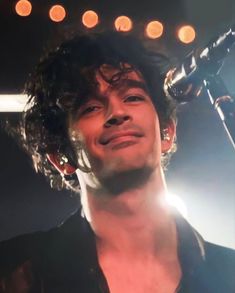 a man with curly hair holding a microphone up to his head and smiling at the camera