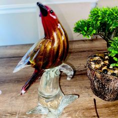 a glass bird sitting on top of a wooden table next to a potted plant