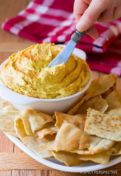 a person dipping hummus into a bowl with tortilla chips on the side