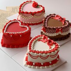 four decorated heart shaped cakes sitting on top of a white table next to an open book