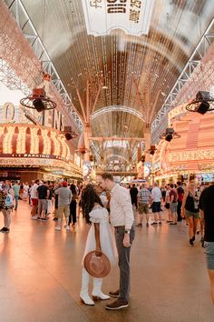 a man and woman are kissing in an indoor market area with many people walking around