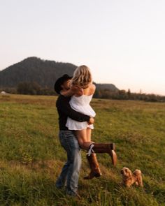 a man and woman hugging in the middle of a field with a dog on leash