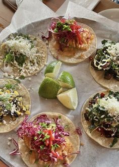 six tacos on a plate with limes, cabbage and shredded cheese in the middle