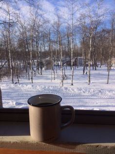 a cup sitting on top of a window sill next to a snow covered field