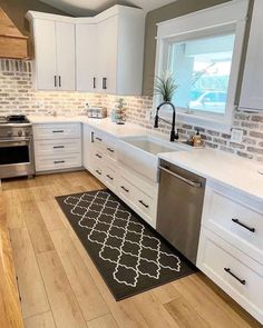 a kitchen with white cabinets and stainless steel appliances in the center, along with an area rug on the floor