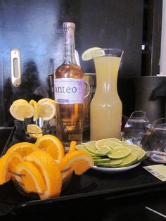 an assortment of fruits and drinks on a counter top with bottles, glasses, and utensils