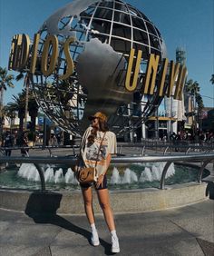 a woman is standing in front of the universal studios sign