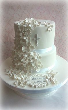 a wedding cake with white flowers and a cross on top is sitting on a plate