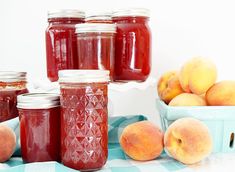 several jars of peach jam sit on a table with fresh peaches in the background