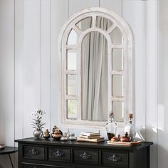 a black dresser topped with a mirror next to a table filled with books and vases