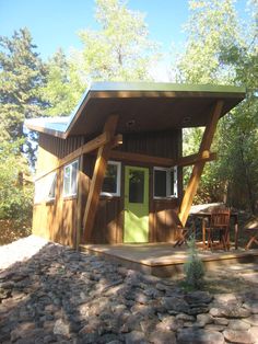 a small wooden cabin in the woods with picnic table and chairs on the front porch