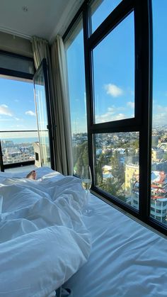 a bed with white sheets and pillows in front of large windows looking out onto the city