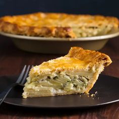 a piece of quiche on a black plate with a fork next to the pie