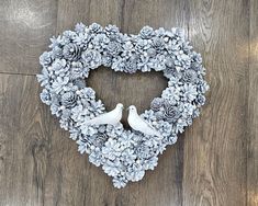 a heart shaped wreath with two doves and pine cones on the front, sitting on a wood floor