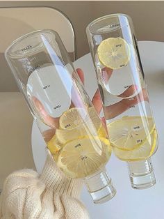 two wine glasses with lemon slices in them on a white table and someone holding one