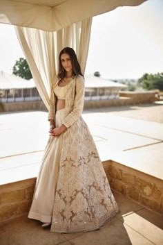 a woman standing in front of a window wearing a white and beige dress with long sleeves