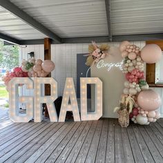 the word grad spelled out in front of balloons and flowers on a wooden floor