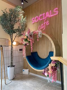 a blue chair sitting under a pink neon sign next to a tree in a room